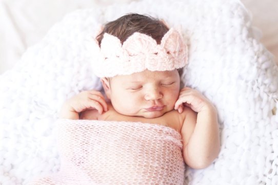 Sweet sleeping tiny newborn princess with a pink crown wrapped in a soft blanket. Cute newborn baby sleeping stock image.