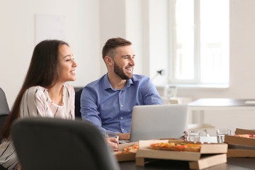 Young people eating pizza at table in office