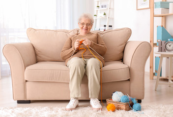 Senior woman sitting on sofa while knitting sweater at home