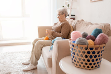 Senior woman sitting on sofa while knitting sweater at home