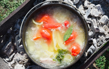 Shurpa soup in a large cast-iron cauldron outdoor. Summer food for hike. Top view.
