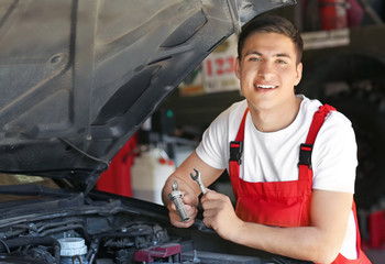 Young auto mechanic repairing car in service center