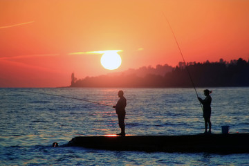 A man with his wife fishing with fishing rods at sea, stand on the pier during sunset.