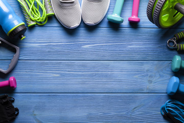 Fitness equipment - sneakers; jumping rope, water bottle and dumbbell on blue wooden board