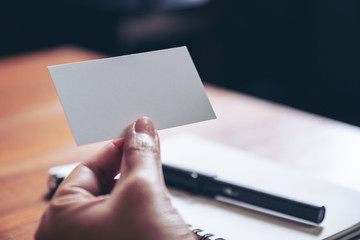 A hand holding white empty business card with notebook on wooden table