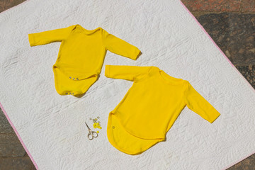 Children bodysuit. Yellow baby bodysuit handmade on light background. Sewing of clothes. Scissors and natural fabric. Copy space