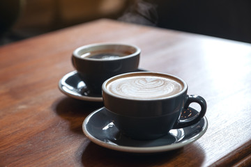 Closeup image of two blue cups of hot latte coffee and Americano coffee on vintage wooden table in cafe