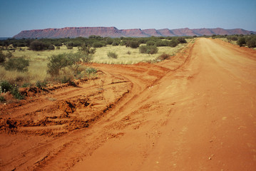 Fototapeta na wymiar Una strada nel deserto australiano con rocce rosse sullo sfondo - Mereenie Loop - Watarrka National Park - Northern Territory - Australia 