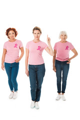 Fototapeta premium women in pink t-shirts with breast cancer awareness ribbons looking at camera and pointing up with finger isolated on white