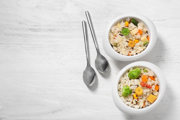 Bowls of tasty rice with vegetables on white wooden table