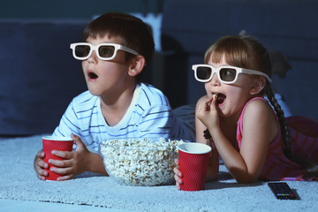 Cute children in 3d glasses watching movie on carpet in evening