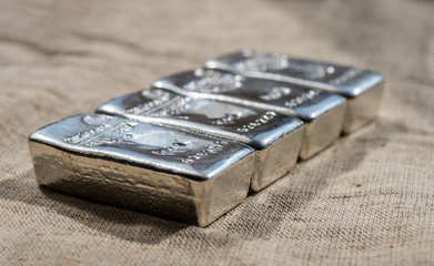 Cast silver bars against the background of the rough texture coarse cloth. Selective focus.