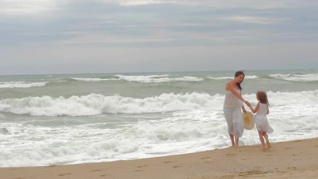 Mom and his beloved daughter are walking along the seashore, holding hands and having fun