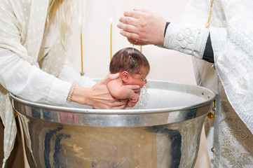 Mother holds child while priest baptizes with holy water