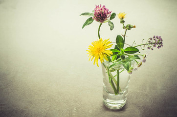 A small bouquet of wildflowers in a glass. Vintage toned image.