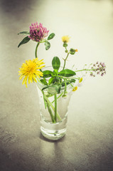 A small bouquet of wildflowers in a glass. Vintage toned image.