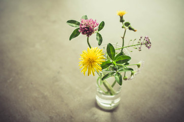 A small bouquet of wildflowers in a glass. Vintage toned image.