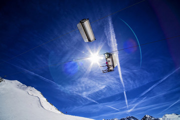 chairlift with two skiers shooted agains the sun, nice lens flare and amazing blue sku background,...