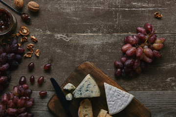 top view of fresh ripe grapes, walnuts, cheese and delicious jam on wooden table