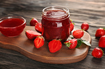 Glass jar and bowl with delicious strawberry jam on wooden table