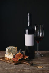 close-up view of bottle and glass of red wine, delicious cheese and figs on wooden board