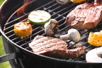 Tasty steaks and vegetables cooking on barbecue grill, closeup