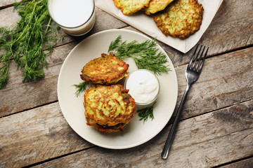 Plate with zucchini pancakes and sauce on wooden table