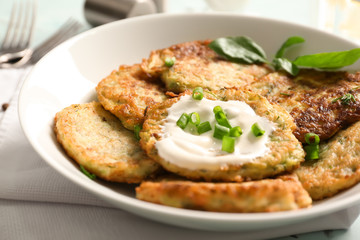 Plate with zucchini pancakes and sauce on table, closeup