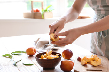 Obraz na płótnie Canvas Woman cutting fresh sweet peaches at wooden table