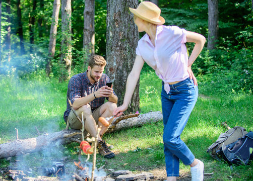 Man busy with smartphone while girl roasting food over fire. Family picnic nature background. Even at vacation he stay in touch with colleagues. Family relaxing at picnic hike or weekend vacation