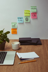 laptop, notebook and pencil on wooden tabletop, paper stickers on wall