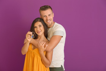 Happy young couple with key from their new house on color background