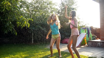 4k footage of two cheerful laughing teenage girls jumping and dancing under rain at house backyard