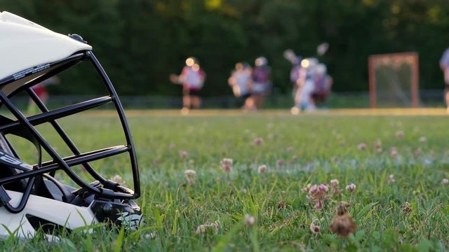 Closeup of lacrosse helmet in the foreground with players and field out of focus in the background.