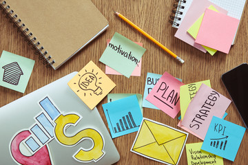 elevated view of stickers with business strategy, paper signs and laptop on table at home