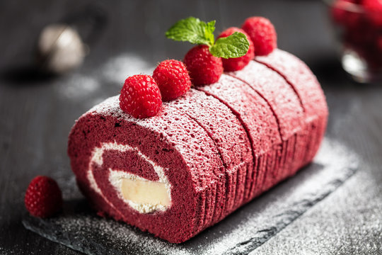 Red velvet Sponge Swiss roll with fresh raspberry and sugar icing on dark background