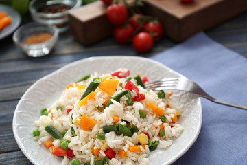 Plate with tasty boiled rice and vegetables on wooden table