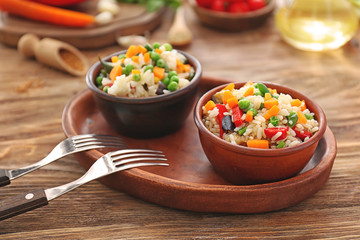 Tasty boiled rice with vegetables in bowls on wooden table