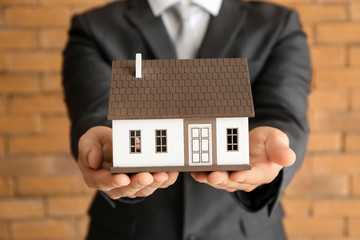 Real estate agent with house model near brick wall, closeup. Mortgage concept