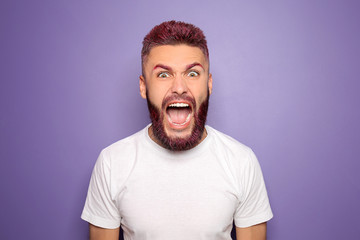 Portrait of angry screaming man with dyed hair and beard on color background