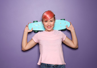 Beautiful young woman with unusual hair holding skateboard on color background