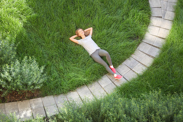 Sporty young woman lying on green grass in park