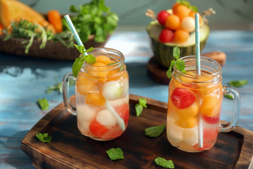 Mason jars of delicious cocktails with melon balls on wooden board