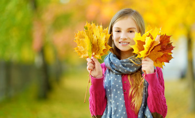 Cute little girl having fun on beautiful autumn day. Happy child playing in autumn park. Kid...