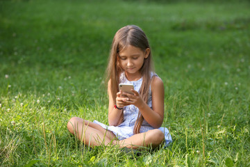 Cute little girl with phone in park on summer day