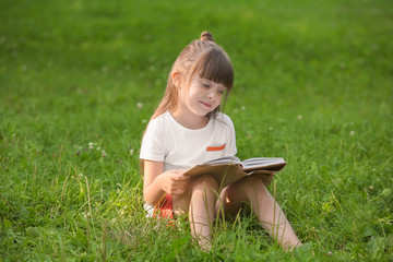 Cute little girl reading book in park on summer day