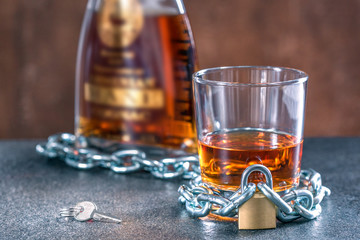 Alcoholism concept,  background with glass and bottle with whiskey locked on a chain.