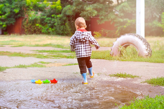 The little boy runs around in puddles in yellow rubber boots and a checkered raincoat.