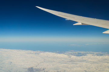 Fototapeta na wymiar Airplane wing flying high above snow mountain area