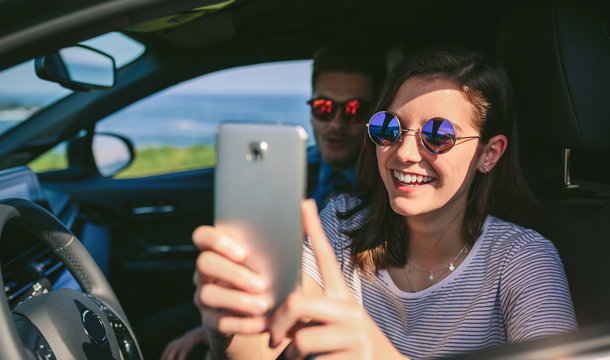 Girl with her boyfriend taking a selfie with the cell phone in the car. Selective focus on girl in background